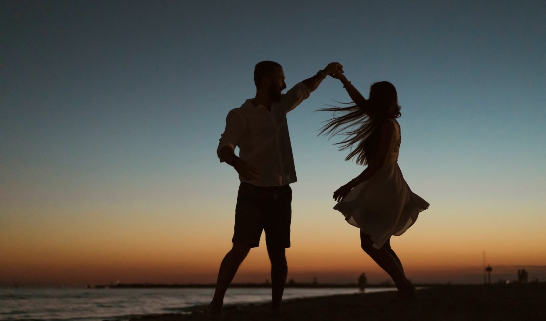a man and woman dancing on a beach at sunset